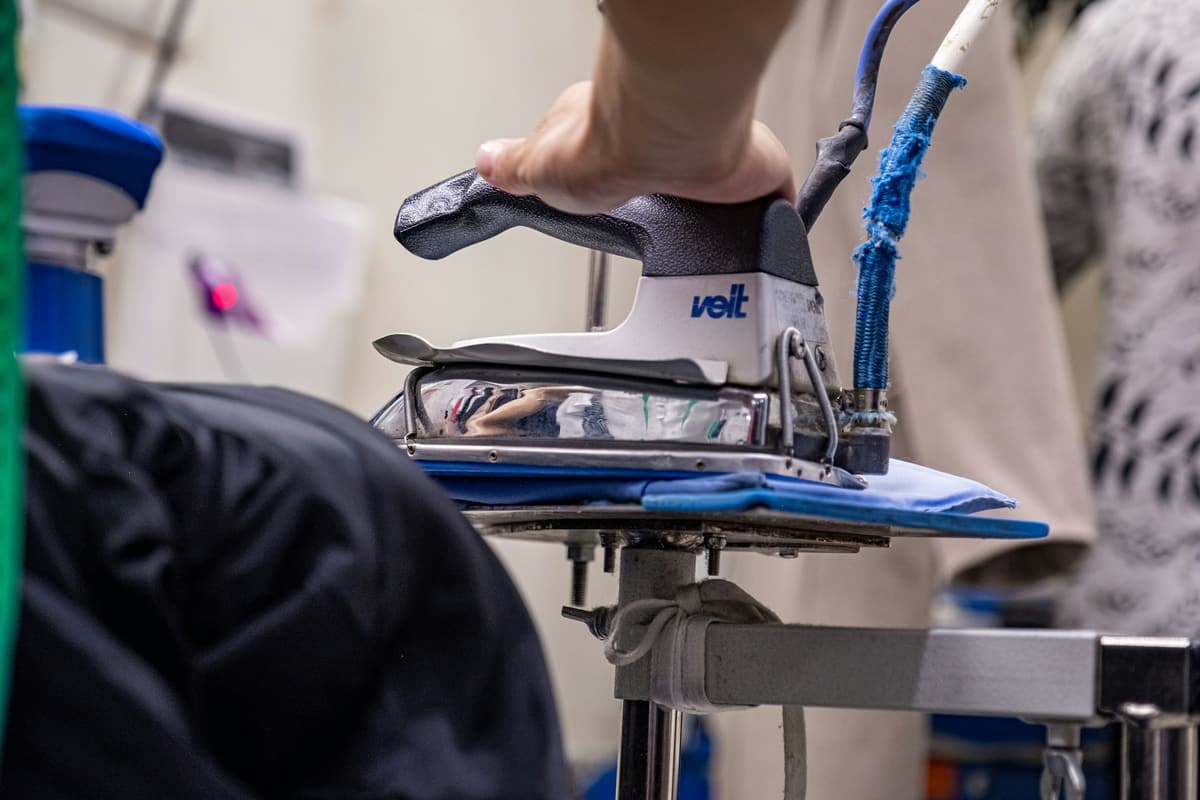 A hand moving an industrial iron over a shirt on the pressing table