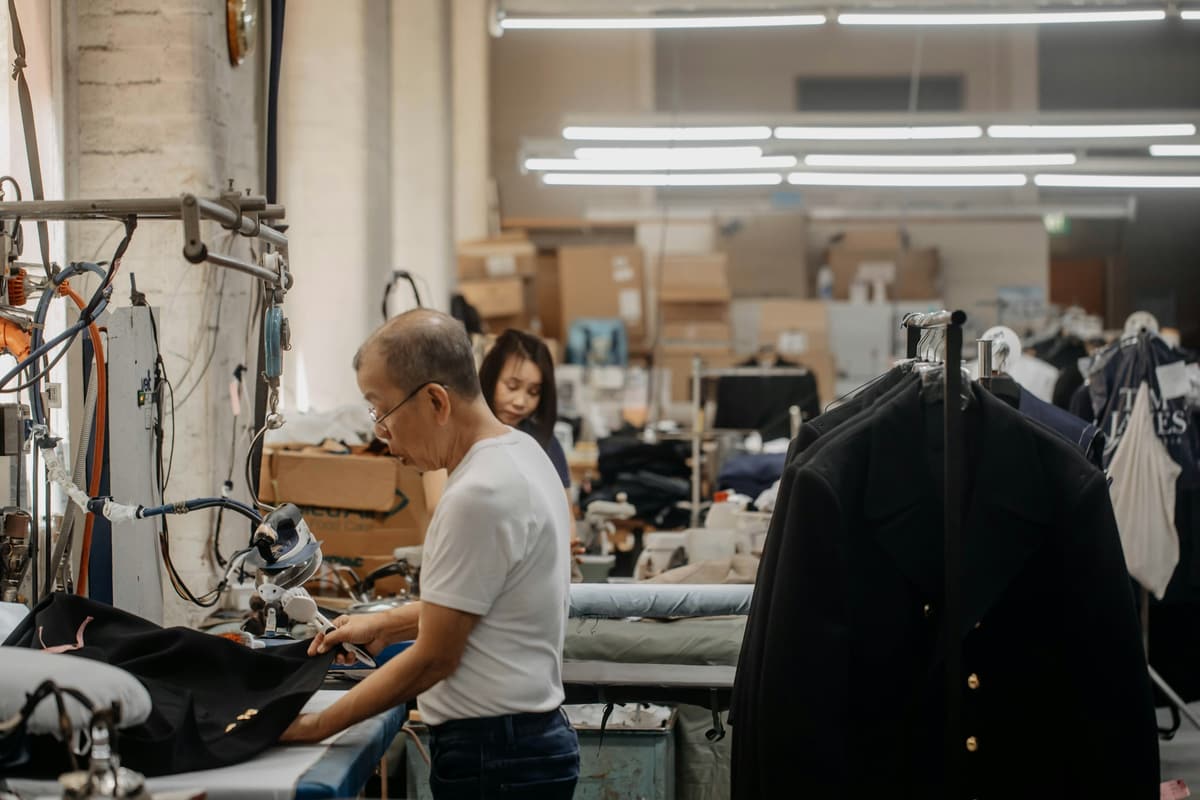 A pressing table in a workroom, a coat hanging on the rail in front of it